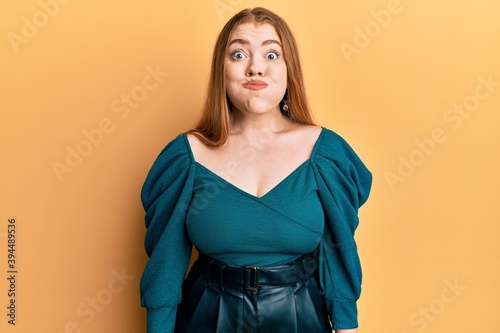 Young beautiful redhead woman wearing elegant and sexy look puffing cheeks with funny face. mouth inflated with air, crazy expression.