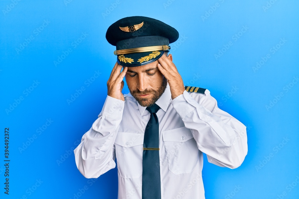 Handsome man with beard wearing airplane pilot uniform with hand on head for pain in head because stress. suffering migraine. Handsome man with beard wearing airplane pilot uniform with hand on head for pain in head because stress. suffering migraine.