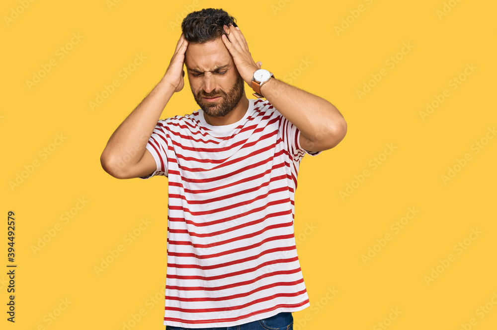 Handsome man with beard wearing striped tshirt suffering from headache desperate and stressed because pain and migraine. hands on head. Handsome man with beard wearing striped tshirt suffering from headache desperate and stressed because pain and migraine. hands on head.
