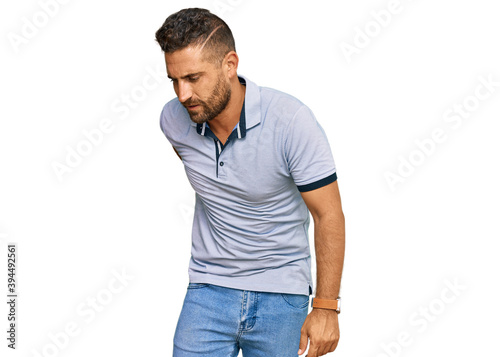 Handsome man with beard wearing casual clothes suffering of backache, touching back with hand, muscular pain