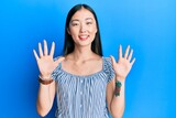 Young chinese woman wearing casual striped t-shirt showing and pointing up with fingers number ten while smiling confident and happy.