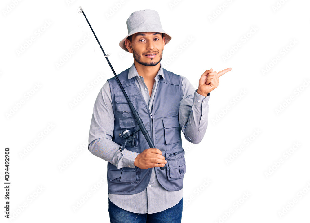 Handsome latin american young man wearing fisherman equipment smiling happy pointing with hand and finger to the side