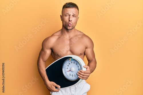 Handsome muscle man holding weight machine to balance weight loss making fish face with mouth and squinting eyes  crazy and comical.
