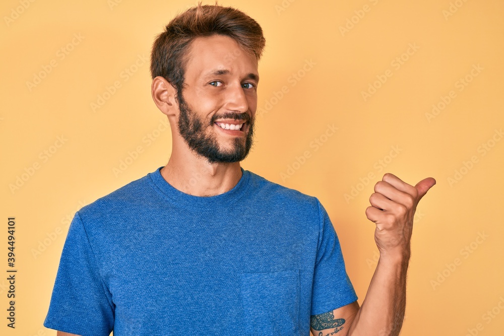 Handsome caucasian man with beard wearing casual clothes smiling with happy face looking and pointing to the side with thumb up. Handsome caucasian man with beard wearing casual clothes smiling with happy face looking and pointing to the side with thumb up.