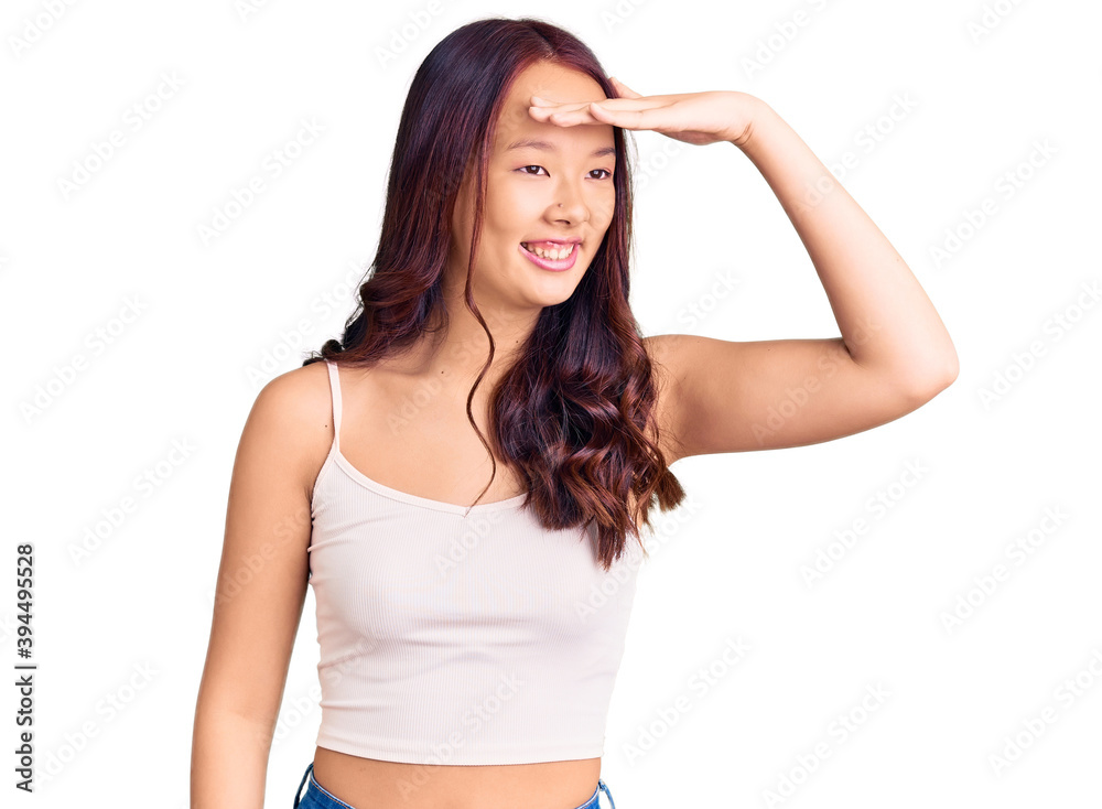 Young beautiful chinese girl wearing casual clothes very happy and smiling looking far away with hand over head. searching concept. Young beautiful chinese girl wearing casual clothes very happy and smiling looking far away with hand over head. searching concept.