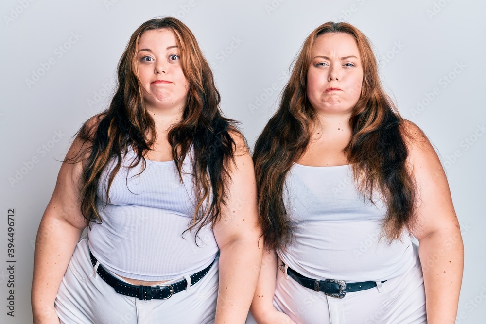 Plus size caucasian sisters woman wearing casual white clothes puffing cheeks with funny face. mouth inflated with air, crazy expression. Plus size caucasian sisters woman wearing casual white clothes puffing cheeks with funny face. mouth inflated with air, crazy expression.