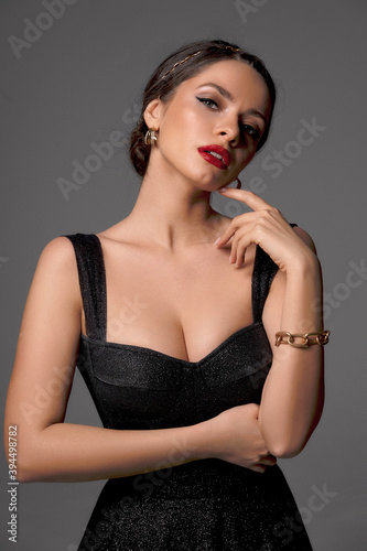 Papier peint Breast up portrait of young elegant sexy woman in black shiny evening dress with decolette against grey background, Beautiful caucasian girl with perfect makeup and hair in bun
