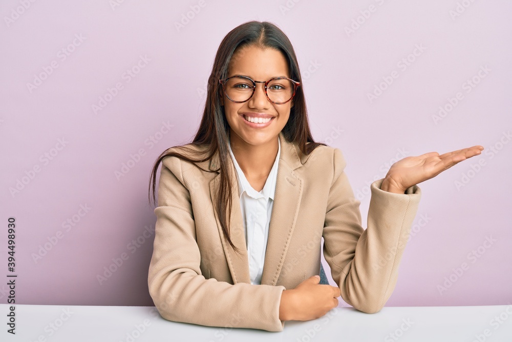 Beautiful hispanic woman working at the office smiling cheerful presenting and pointing with palm of hand looking at the camera. Beautiful hispanic woman working at the office smiling cheerful presenting and pointing with palm of hand looking at the camera.