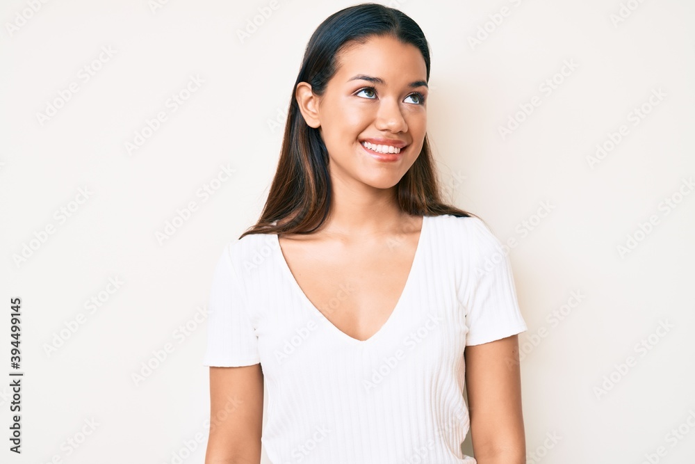 Young beautiful latin girl wearing casual white tshirt looking to side, relax profile pose with natural face and confident smile. Young beautiful latin girl wearing casual white tshirt looking to side, relax profile pose with natural face and confident smile.