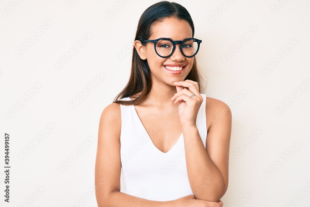 Young beautiful latin girl wearing casual clothes and glasses smiling looking confident at the camera with crossed arms and hand on chin. thinking positive. Young beautiful latin girl wearing casual clothes and glasses smiling looking confident at the camera with crossed arms and hand on chin. thinking positive.