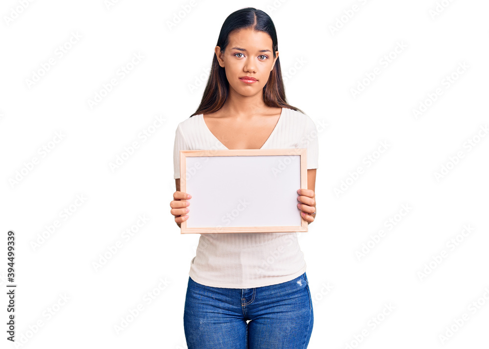 Young beautiful latin girl holding empty white chalkboard thinking attitude and sober expression looking self confident