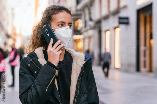New normal. Teenager talking on the phone with a coronavirus mask. Young girl talking on the phone. Mask against covid. Teenager with face mask. Pandemic. Teenager talking. © Tomaspf_