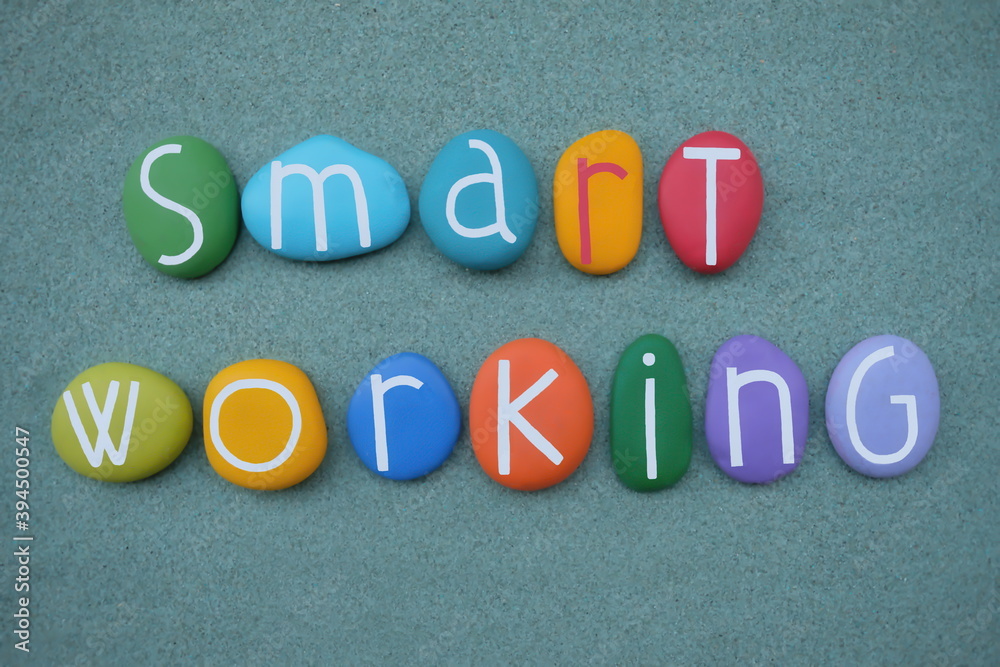 Smart working, new model of work text composed with multicolored stone letters over green sand Smart working, new model of work text composed with multicolored stone letters over green sand