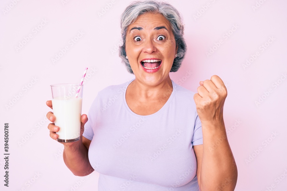 Senior hispanic woman holding glass of milk screaming proud, celebrating victory and success very excited with raised arms Senior hispanic woman holding glass of milk screaming proud, celebrating victory and success very excited with raised arms