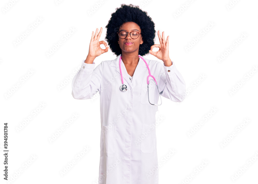 Young african american woman wearing doctor coat and stethoscope relaxed and smiling with eyes closed doing meditation gesture with fingers. yoga concept. Young african american woman wearing doctor coat and stethoscope relaxed and smiling with eyes closed doing meditation gesture with fingers. yoga concept.