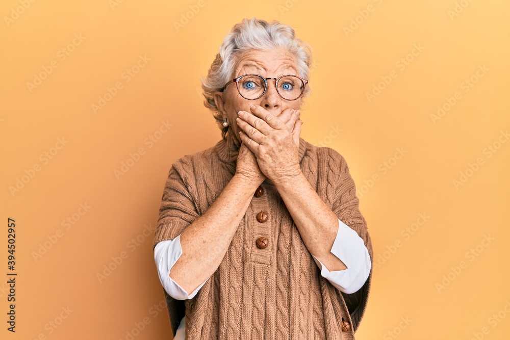Senior grey-haired woman wearing casual clothes and glasses shocked covering mouth with hands for mistake. secret concept. Senior grey-haired woman wearing casual clothes and glasses shocked covering mouth with hands for mistake. secret concept.