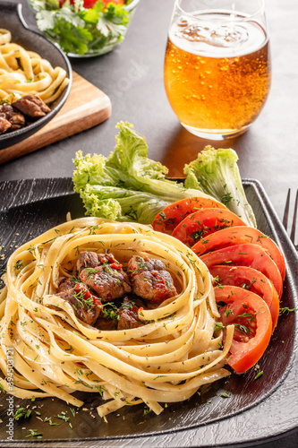 Fettuccine pasta with pieces of beef, tomatoes and lettuce.