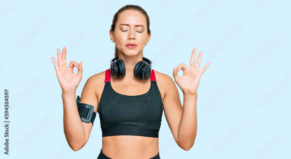 Beautiful blonde woman wearing gym clothes and using headphones relaxed and smiling with eyes closed doing meditation gesture with fingers. yoga concept. Beautiful blonde woman wearing gym clothes and using headphones relaxed and smiling with eyes closed doing meditation gesture with fingers. yoga concept.