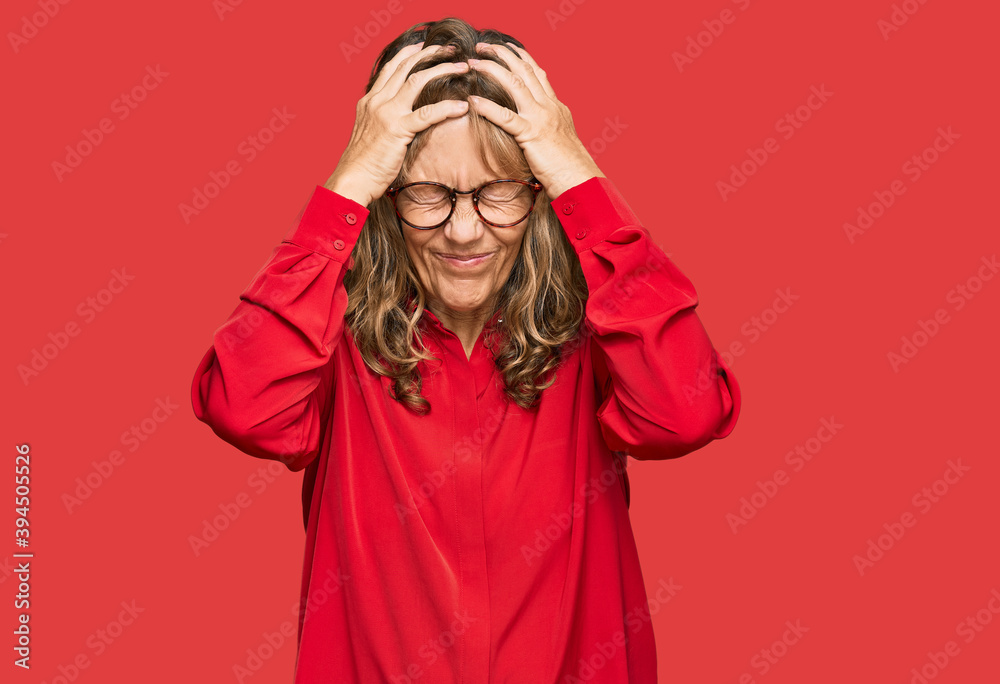 Middle age blonde woman wearing casual shirt over red background suffering from headache desperate and stressed because pain and migraine. hands on head. Middle age blonde woman wearing casual shirt over red background suffering from headache desperate and stressed because pain and migraine. hands on head.