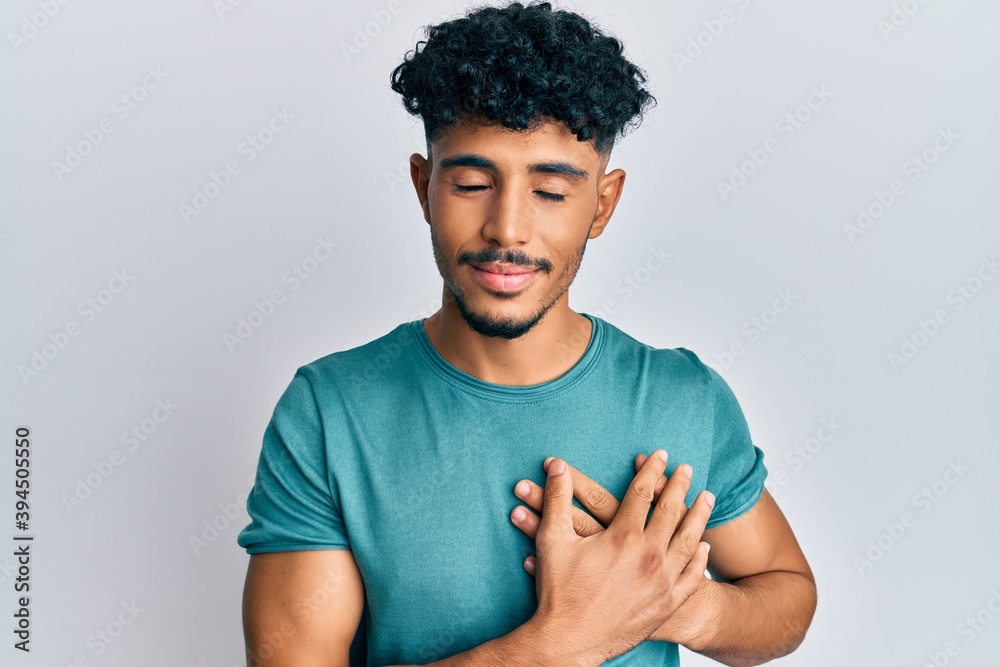 Young arab handsome man wearing casual clothes smiling with hands on chest with closed eyes and grateful gesture on face. health concept.