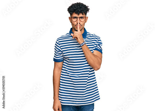 Young arab man wearing casual clothes and glasses asking to be quiet with finger on lips. silence and secret concept.