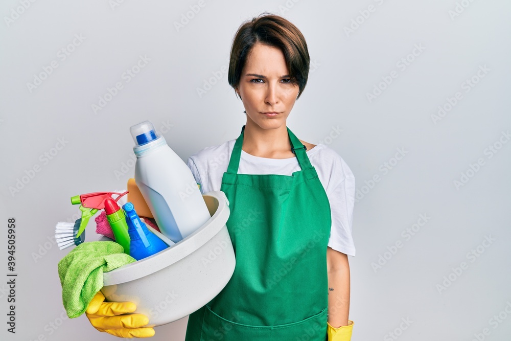 Young brunette woman with short hair wearing apron holding cleaning products skeptic and nervous, frowning upset because of problem. negative person. Young brunette woman with short hair wearing apron holding cleaning products skeptic and nervous, frowning upset because of problem. negative person.