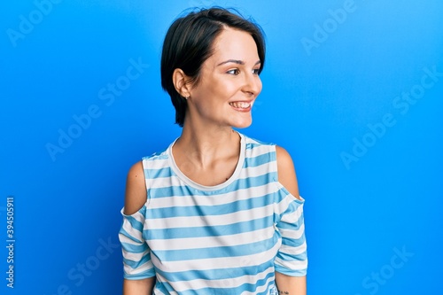 Young brunette woman with short hair wearing casual striped t-shirt looking away to side with smile on face, natural expression. laughing confident. © Krakenimages.com