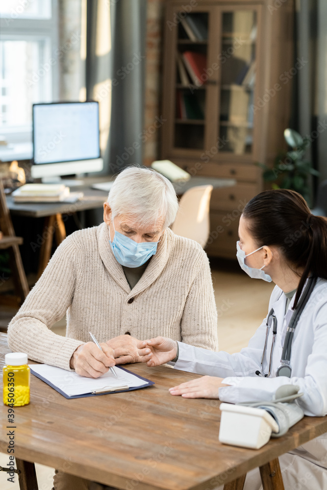 Obraz premium Sick senior male patient in mask and casualwear signing medical paper