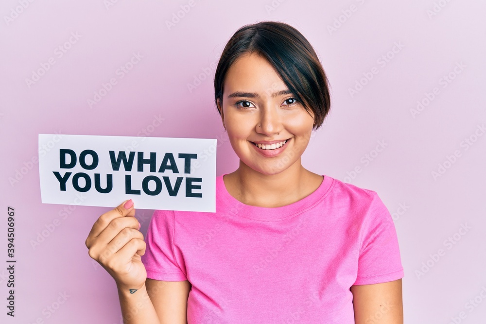 Beautiful young woman with short hair holding paper with do what you love text looking positive and happy standing and smiling with a confident smile showing teeth Beautiful young woman with short hair holding paper with do what you love text looking positive and happy standing and smiling with a confident smile showing teeth
