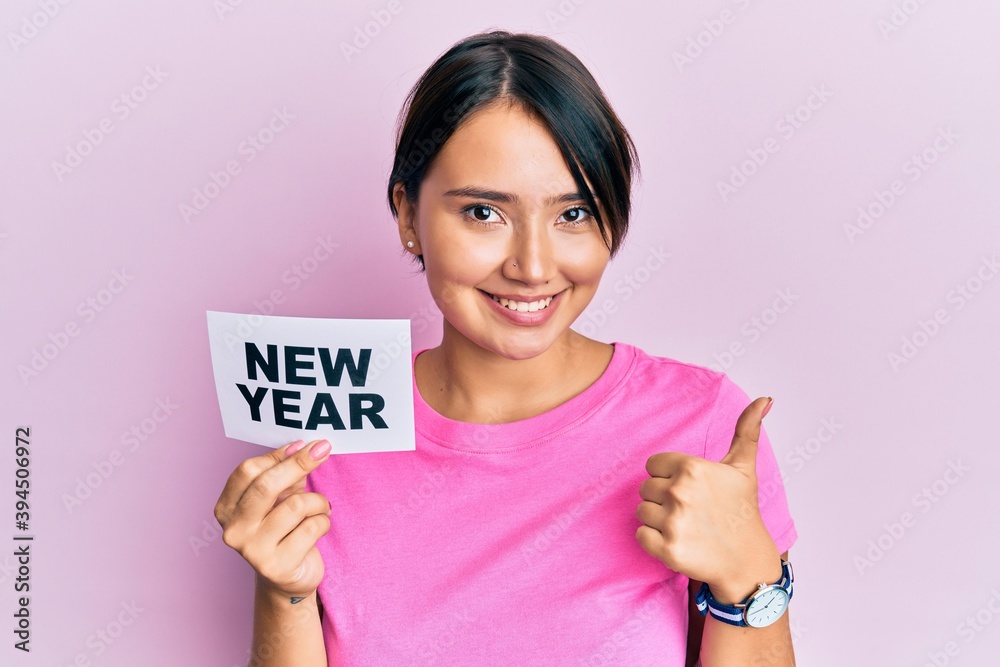 Beautiful young woman with short hair holding new year message on paper smiling happy and positive, thumb up doing excellent and approval sign Beautiful young woman with short hair holding new year message on paper smiling happy and positive, thumb up doing excellent and approval sign