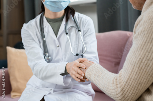 Hands of female doctor in whitecoat and protective mask supporting sick man