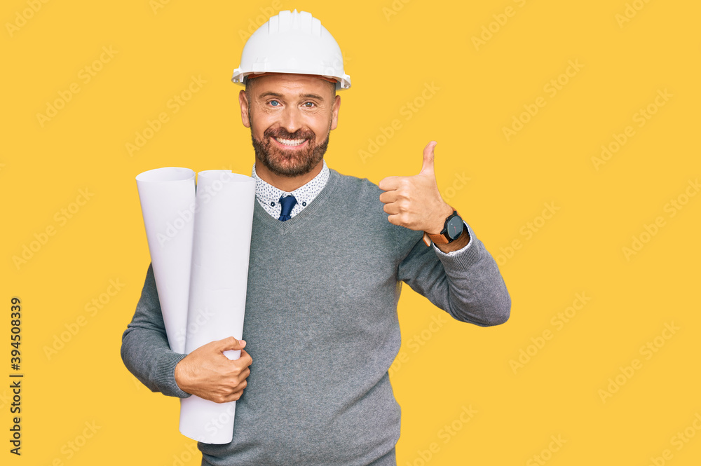 Handsome middle age man holding paper blueprints smiling happy and positive, thumb up doing excellent and approval sign