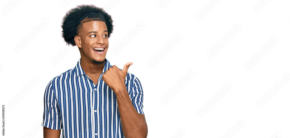 African american man with afro hair wearing casual clothes smiling with happy face looking and pointing to the side with thumb up. African american man with afro hair wearing casual clothes smiling with happy face looking and pointing to the side with thumb up.