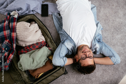 Young smiling man packing clothes into travel bag. Man preparing for the trip..