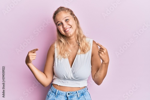 Young blonde girl wearing casual clothes looking confident with smile on face  pointing oneself with fingers proud and happy.