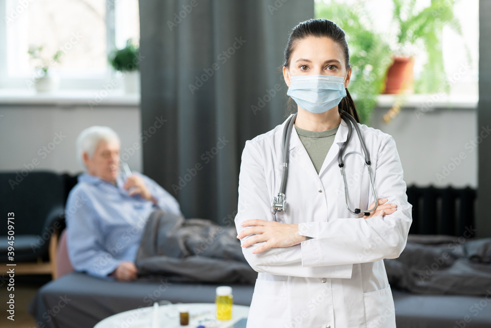 Young pretty doctor in whitecoat and protective mask crossing her arms by chest