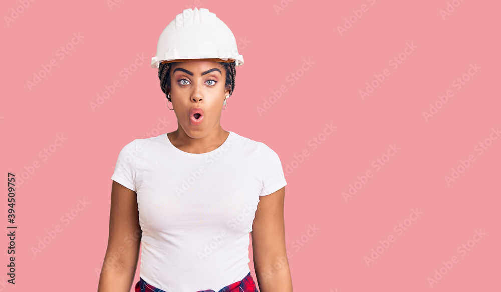 Young african american woman with braids wearing hardhat and builder clothes scared and amazed with open mouth for surprise, disbelief face