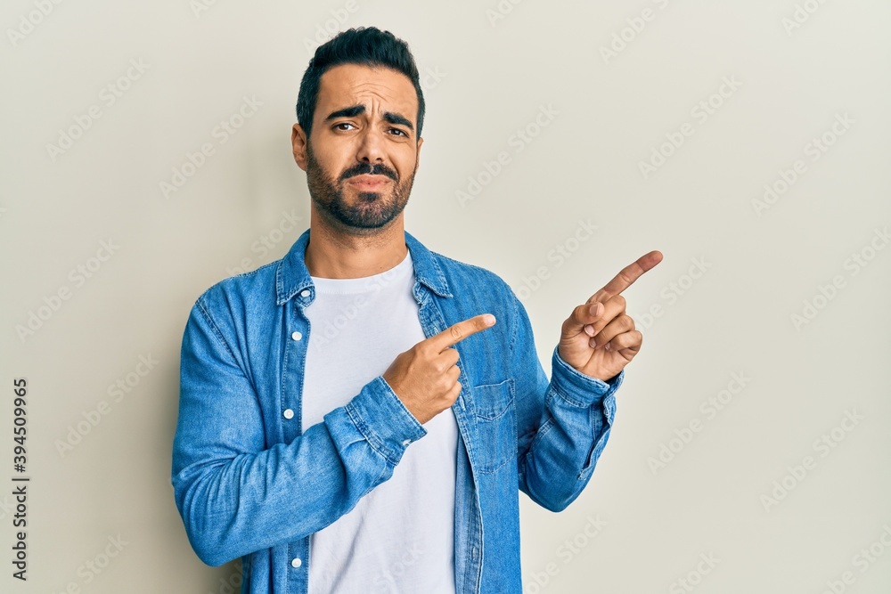Young hispanic man with beard pointing with fingers to the side looking at the camera blowing a kiss being lovely and sexy. love expression. Young hispanic man with beard pointing with fingers to the side looking at the camera blowing a kiss being lovely and sexy. love expression.
