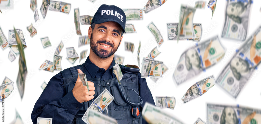 Young hispanic man wearing police uniform doing happy thumbs up gesture with hand. approving expression looking at the camera showing success. Young hispanic man wearing police uniform doing happy thumbs up gesture with hand. approving expression looking at the camera showing success.