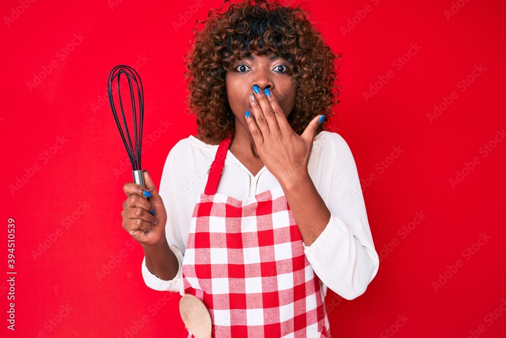 Young african american woman wearing apron holding whisk covering mouth with hand, shocked and afraid for mistake. surprised expression Young african american woman wearing apron holding whisk covering mouth with hand, shocked and afraid for mistake. surprised expression