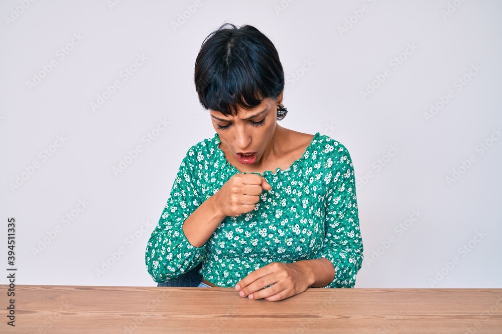 Beautiful brunettte woman wearing casual clothes sitting on the table feeling unwell and coughing as symptom for cold or bronchitis. health care concept. Beautiful brunettte woman wearing casual clothes sitting on the table feeling unwell and coughing as symptom for cold or bronchitis. health care concept.