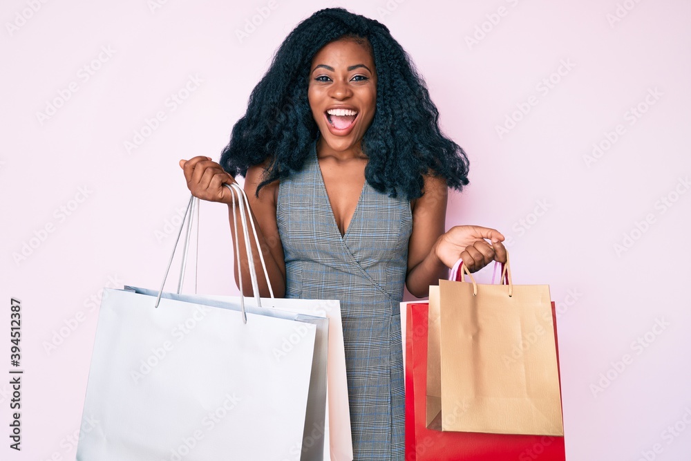 Young african american woman holding shopping bags celebrating crazy and amazed for success with open eyes screaming excited. Young african american woman holding shopping bags celebrating crazy and amazed for success with open eyes screaming excited.
