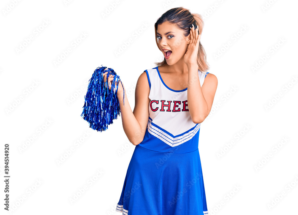 Young beautiful woman wearing cheerleader uniform smiling with hand over ear listening an hearing to rumor or gossip. deafness concept. Young beautiful woman wearing cheerleader uniform smiling with hand over ear listening an hearing to rumor or gossip. deafness concept.