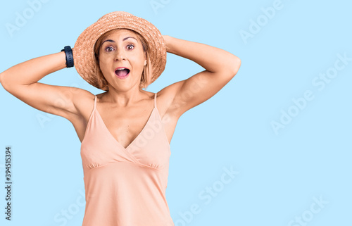 Young blonde woman wearing summer hat crazy and scared with hands on head, afraid and surprised of shock with open mouth