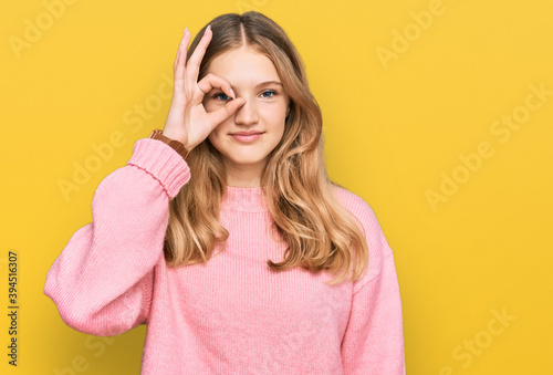 Beautiful young caucasian girl wearing casual winter sweater doing ok gesture with hand smiling, eye looking through fingers with happy face.