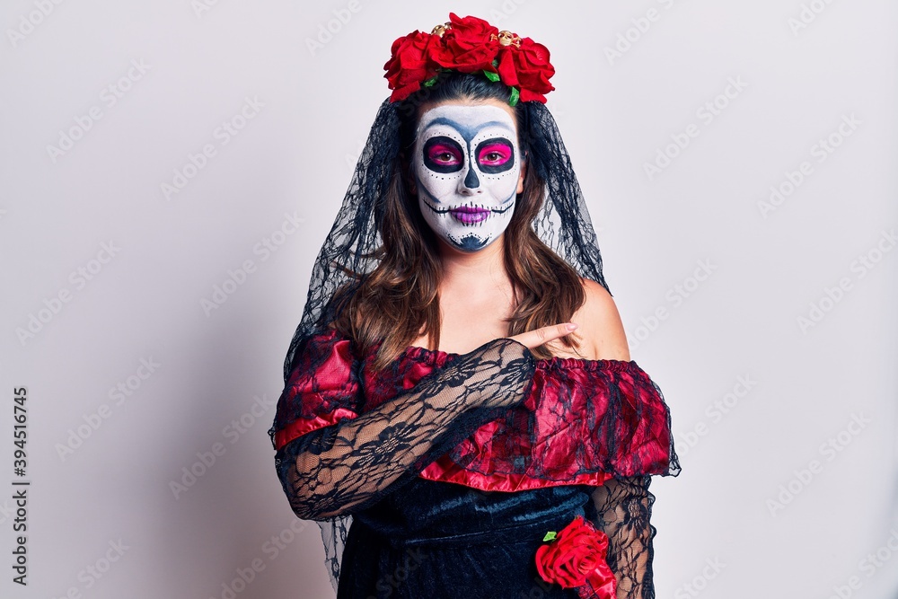 Young woman wearing day of the dead costume over white cheerful with a smile on face pointing with hand and finger up to the side with happy and natural expression