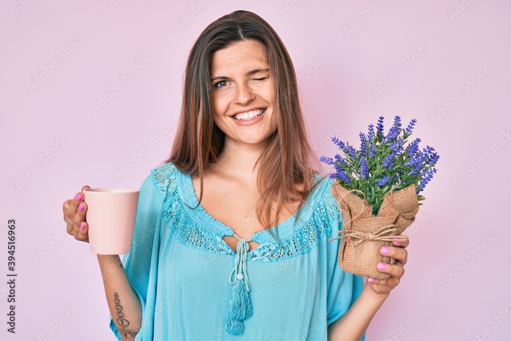 Beautiful caucasian woman drinking a cup of infused lavender winking looking at the camera with sexy expression, cheerful and happy face. Beautiful caucasian woman drinking a cup of infused lavender winking looking at the camera with sexy expression, cheerful and happy face.