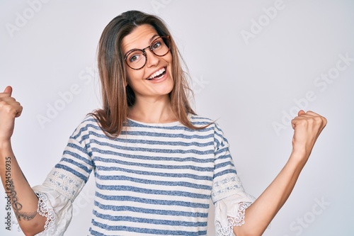 Beautiful caucasian woman wearing casual clothes and glasses screaming proud, celebrating victory and success very excited with raised arms