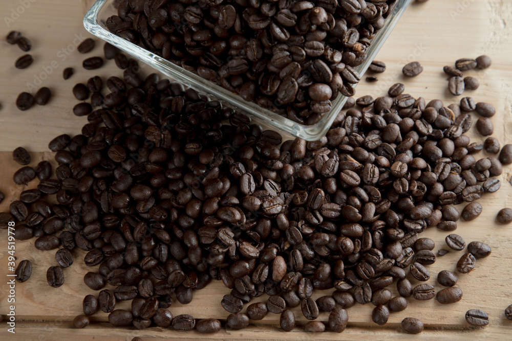 Café negro en grano sobre madera y en un recipiente de cristal Café negro en grano sobre madera y en un recipiente de cristal