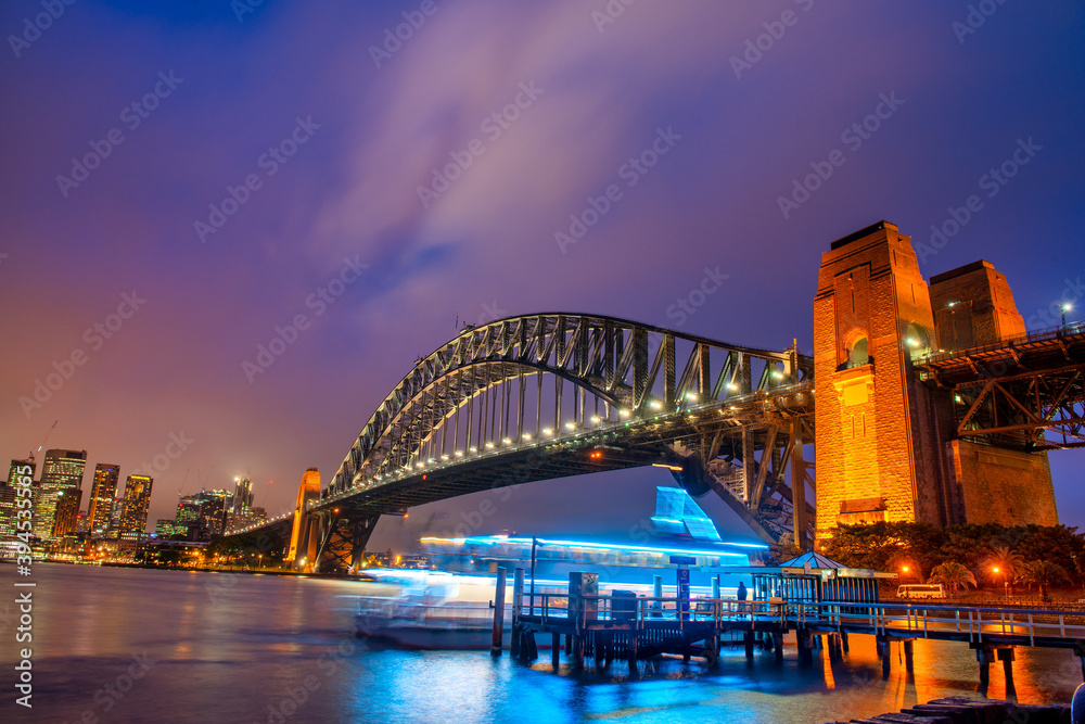 Naklejka premium Sydney Harbour Bridge at night with ferry boat crossing and city skyline